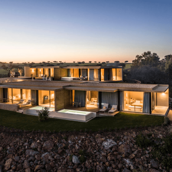 Vista panorâmica da Herdade da Malhadinha Nova, uma propriedade pitoresca em Portugal. A paisagem exibe vinhas ondulantes, olivais e a beleza tranquila da região do Alentejo. A mistura harmoniosa da natureza e da arquitetura da propriedade é evidente, criando uma atmosfera serena e convidativa. Uma viagem visual que capta a essência deste destino idílico, convidando os hóspedes a saborear a beleza e a tranquilidade da Herdade da Malhadinha Nova