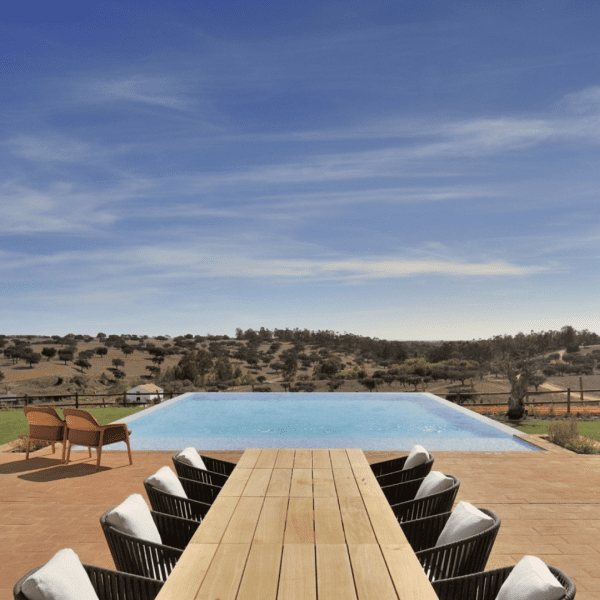 Vista panorâmica da Herdade da Malhadinha Nova, uma propriedade pitoresca em Portugal. A paisagem exibe vinhas ondulantes, olivais e a beleza tranquila da região do Alentejo. A mistura harmoniosa da natureza e da arquitetura da propriedade é evidente, criando uma atmosfera serena e convidativa. Uma viagem visual que capta a essência deste destino idílico, convidando os hóspedes a saborear a beleza e a tranquilidade da Herdade da Malhadinha Nova